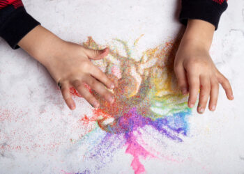 Hand crafting with colorful sand close up. Motor skills, child creativity concept.