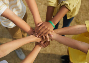 Top view close up at multi-ethnic group of children stacking hands while standing in circle outdoors, concept of friendship and unity