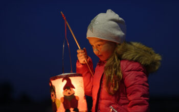 Portrait of little girl with lighted paper lantern on St. Martin's Day at twilight